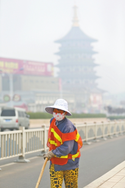 近日，在古都洛陽(yáng)，環(huán)衛(wèi)工人身后的“天堂”被霧霾籠罩著。