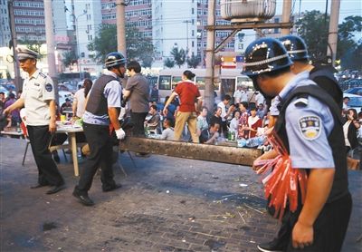 6月13日晚8點，朝陽路和青年路交叉口西側(cè)，一次聯(lián)合執(zhí)法行動中，輔警與協(xié)管抬走商戶的燒烤用具。新京報記者 尹亞飛 攝