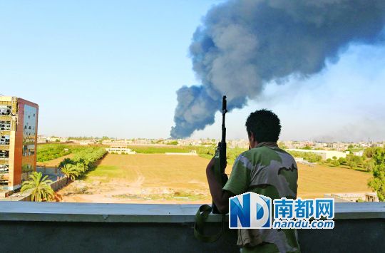 2日，利比亞首都的黎波里，一民兵武裝成員眺望被火箭彈擊中的儲油罐冒出濃煙。