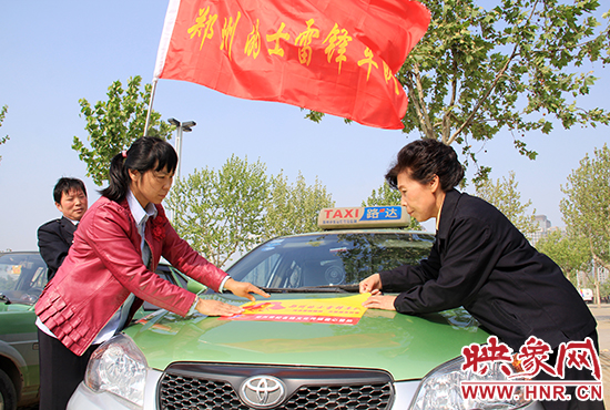 　　授旗結(jié)束后，首都的士雷鋒車隊王鳳進隊長（右）與鄭州的的哥的姐在車身上貼上標(biāo)識。