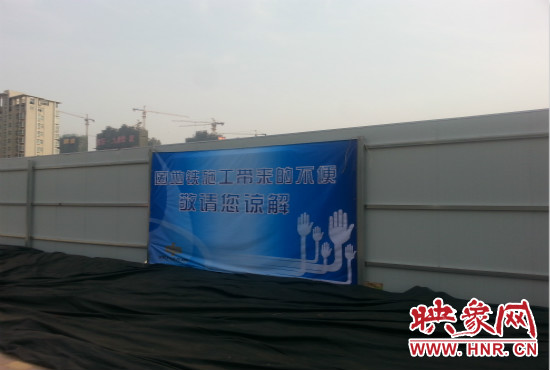 道路南側(cè)圍起了白色的圍擋，墻上標(biāo)示著“因地鐵施工帶來的不便敬請您諒解”的提示牌。