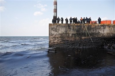 昨日，山東青島，清污人員正在海邊清理油污。