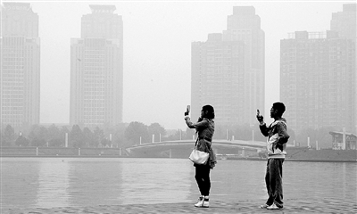 29日中午，鄭東新區(qū)如意湖畔，兩個(gè)年輕人拍攝霧霾中的景色。 鄭州晚報(bào)記者 馬健 圖