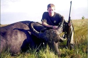 哈里王子手持獵槍，蹲在一頭遭到獵殺的水牛旁邊