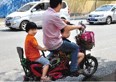 周先生騎著一輛低矮的電動(dòng)車帶著一對(duì)兒女，很不安全。