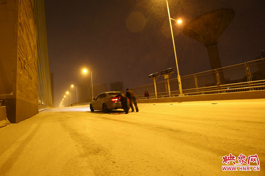 雪天路滑，汽車上橋打滑，兩名“推車人”幫助一輛私家車上坡。