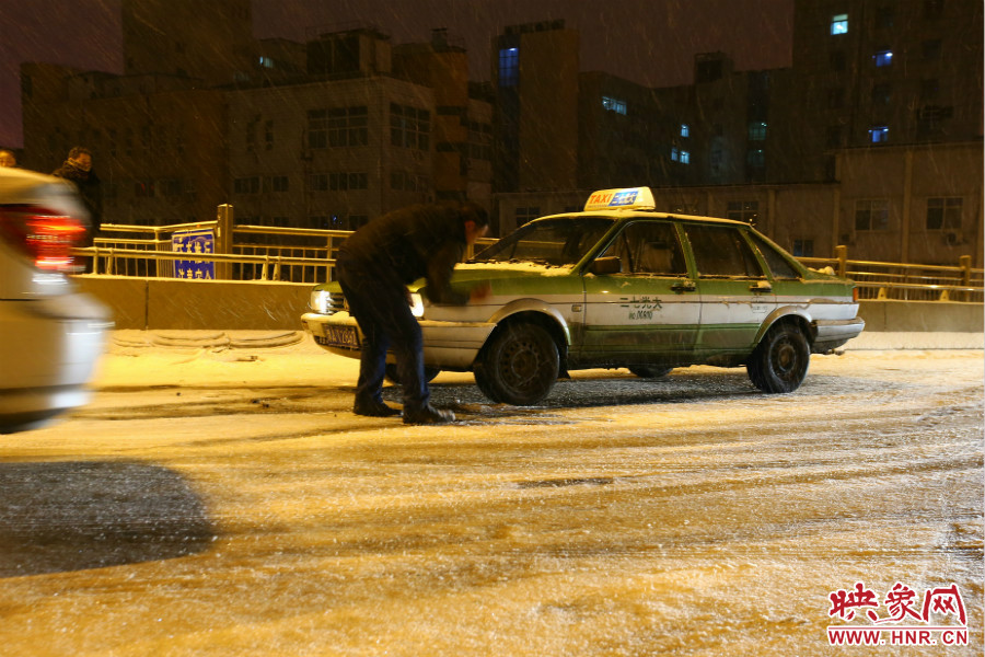 一位出租車司機在車輪前灑上雪，希望能增加輪胎的摩擦力。