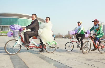 氣球和鮮花裝點(diǎn)的雙人自行車，新郎郝幸福載著美麗新娘回家。