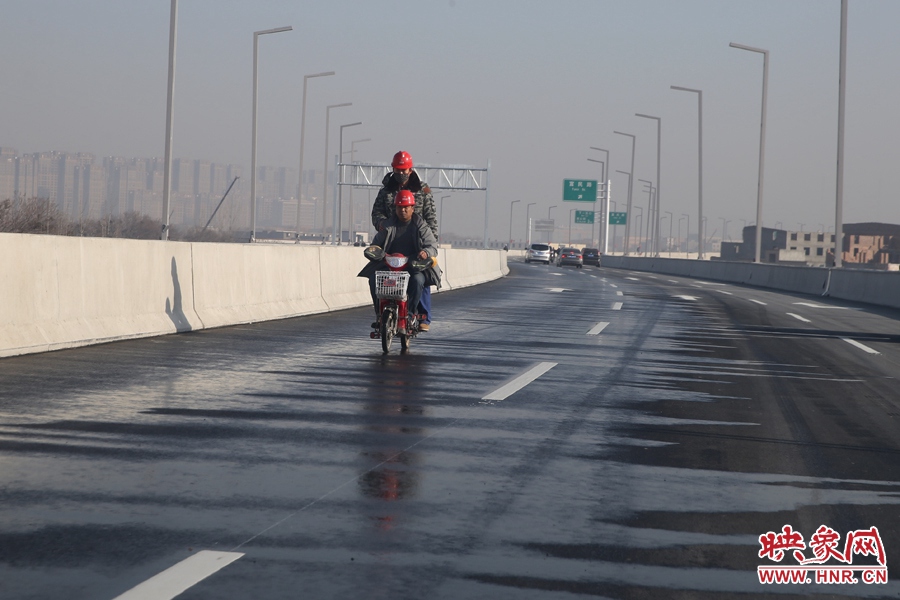 兩名工人騎車經(jīng)過灑水養(yǎng)護(hù)路面。