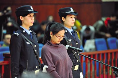 被告人盧梅低著頭，站在朝陽法院刑事審判庭的被告席上。